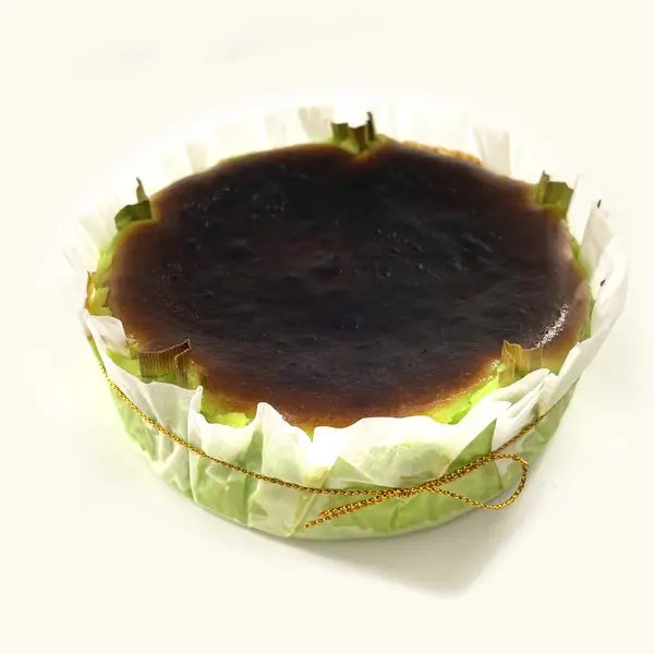 Whole Pandan Burnt Cheesecake in fluted parchment with gold string, green sides