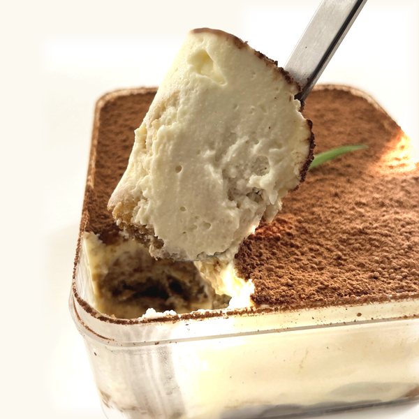 A spoon lifting a scoop of tiramisu cream and ladyfinger out of the tub
